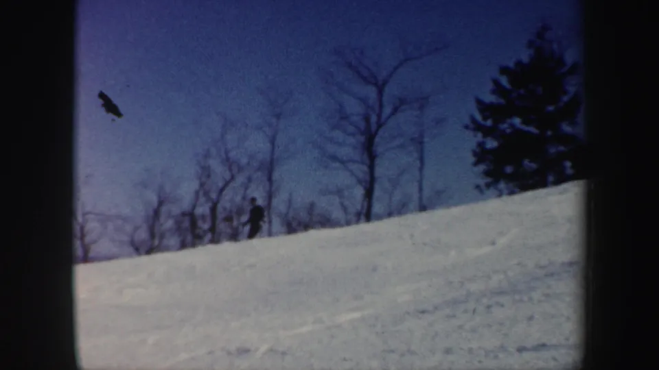 1962 Vermont 8mm frame with a distant skier on the snow, winter trees, and a dark airborne shape or film mark above.