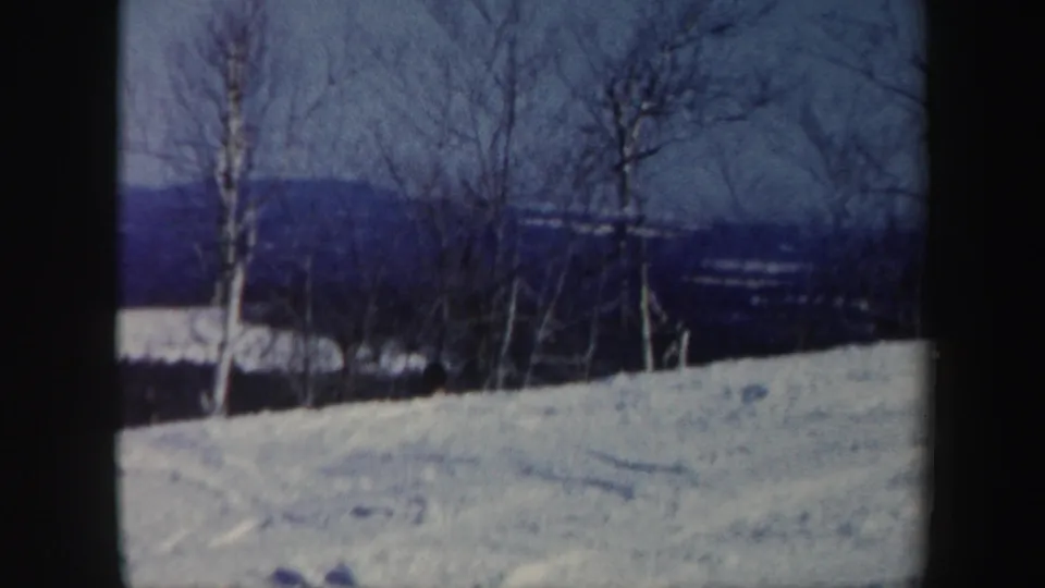 1962 Vermont 8mm frame of a snow-covered hillside bordered by leafless trees and distant wooded ridges.