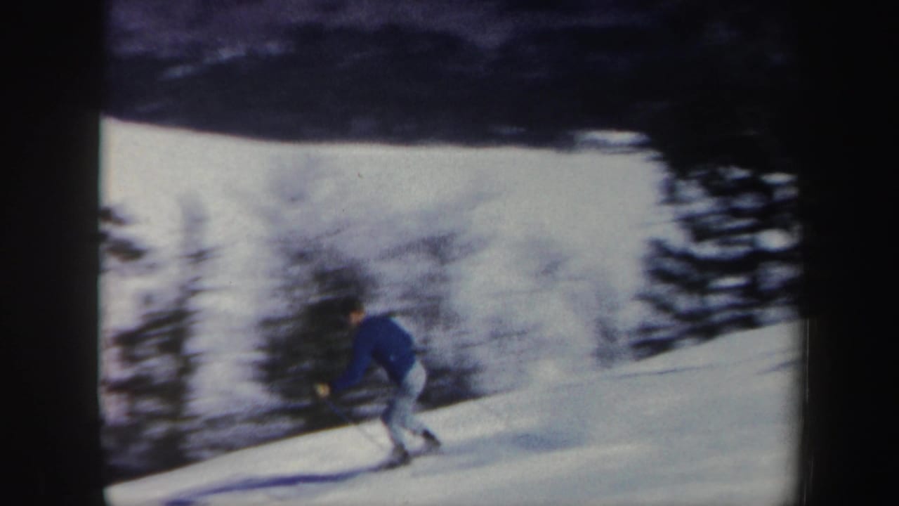 Skier moves across a snowy rise near blurred trees and dark frame edges.