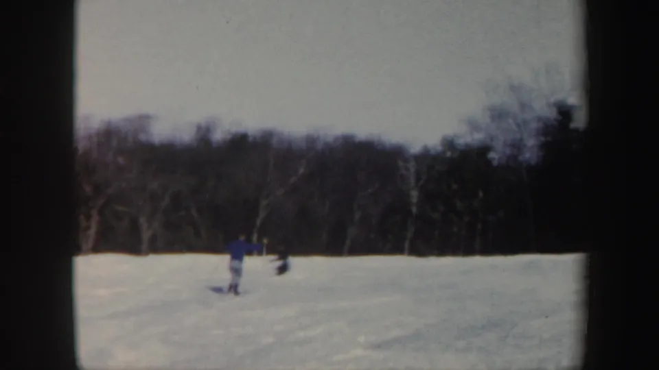 1962 Vermont 8mm frame showing a distant skier in blue moving across a snow-covered slope bordered by winter trees.
