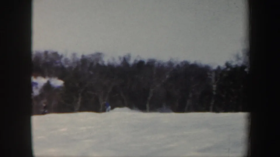 1962 Vermont home-movie frame showing a small skier on a snowy rise against a dark winter tree line.