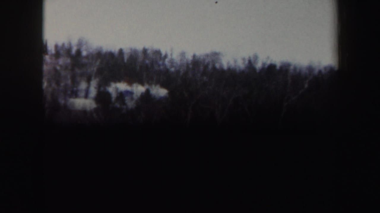 Snowy hillside with treeline and dark film borders visible.