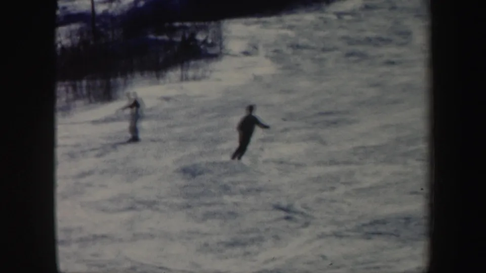 Two distant skiers descend a snowy Vermont hillside in a faded 1962 8mm home-movie frame.