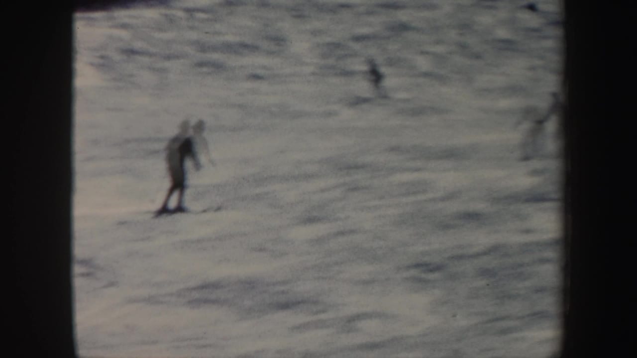 A distant skier descends a snow-covered Vermont hill in 1962 home-movie footage, with soft focus and dark frame edges.