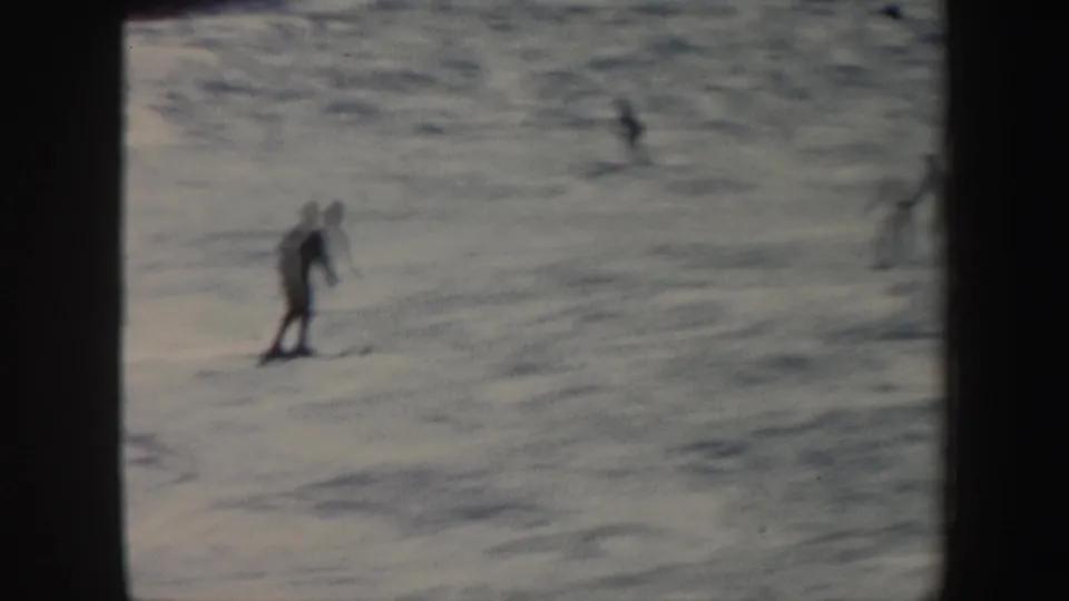 A distant skier descends a snow-covered Vermont hill in 1962 home-movie footage, with soft focus and dark frame edges.