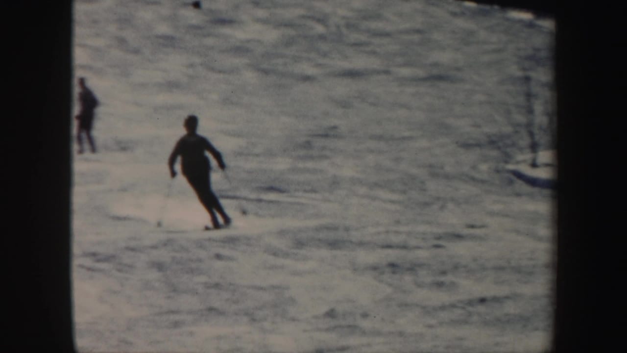 Skiers move down a Vermont snow slope, including a foreground figure turning on long skis in 1962 8mm footage.