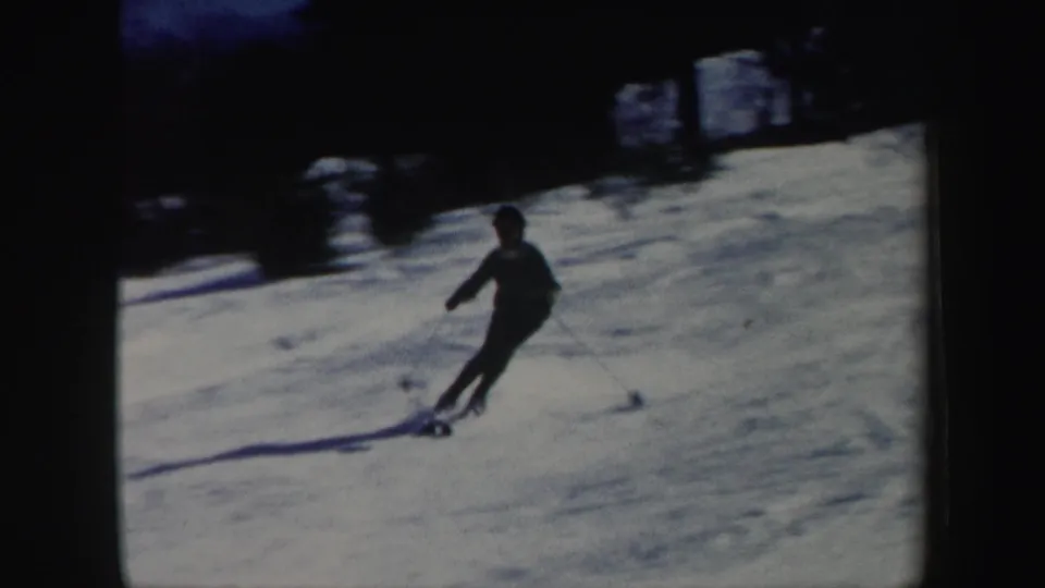 A skier carves across a snowy Vermont hillside near a dark tree line, shown in grainy 1962 8mm home-movie footage.