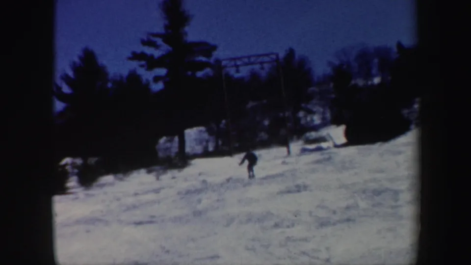 1962 Vermont 8mm frame showing a distant skier moving down a snow-covered slope bordered by trees.