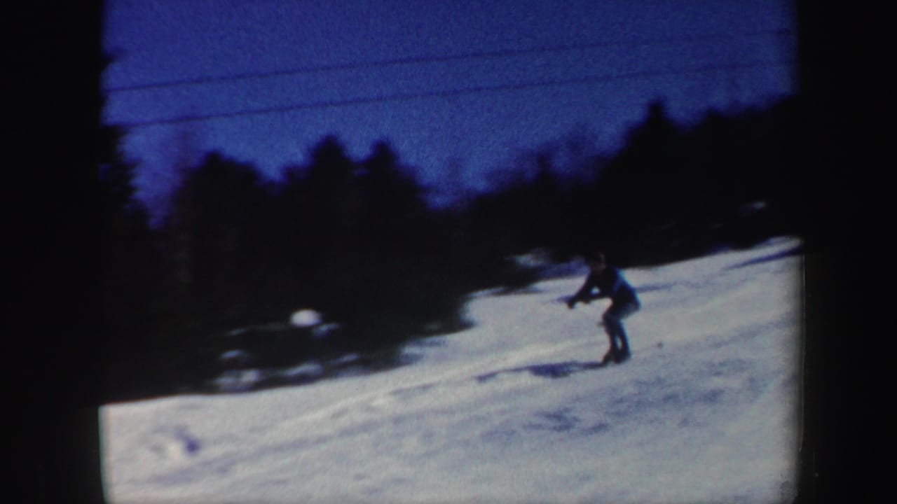 A skier in dark winter clothing traverses a Vermont snow slope in soft, grainy 8mm color.