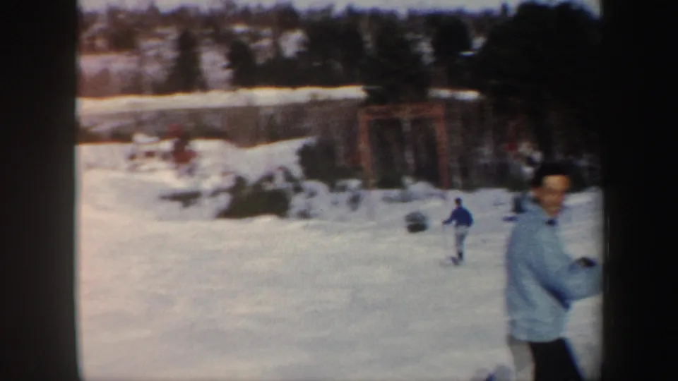 Vermont ski-slope view with a distant skier, slope-side structures, trees, and a nearby person partly in frame.