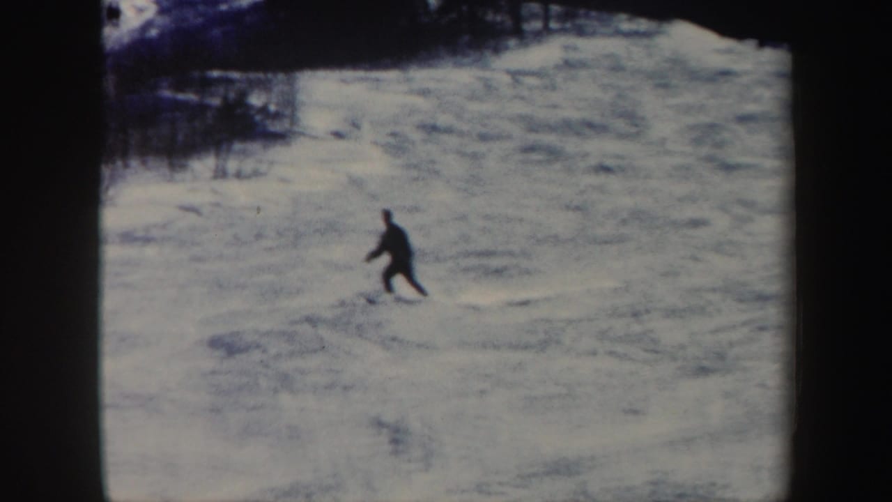 Lone skier crossing a snowy slope with trees along the upper edge.