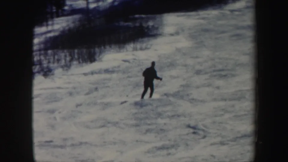 1962 Vermont ski footage frame with a single dark-clad skier on a bright snowfield bordered by trees.