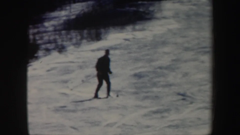 1962 Vermont frame showing a lone skier from behind on a snow-covered slope below a wooded edge.