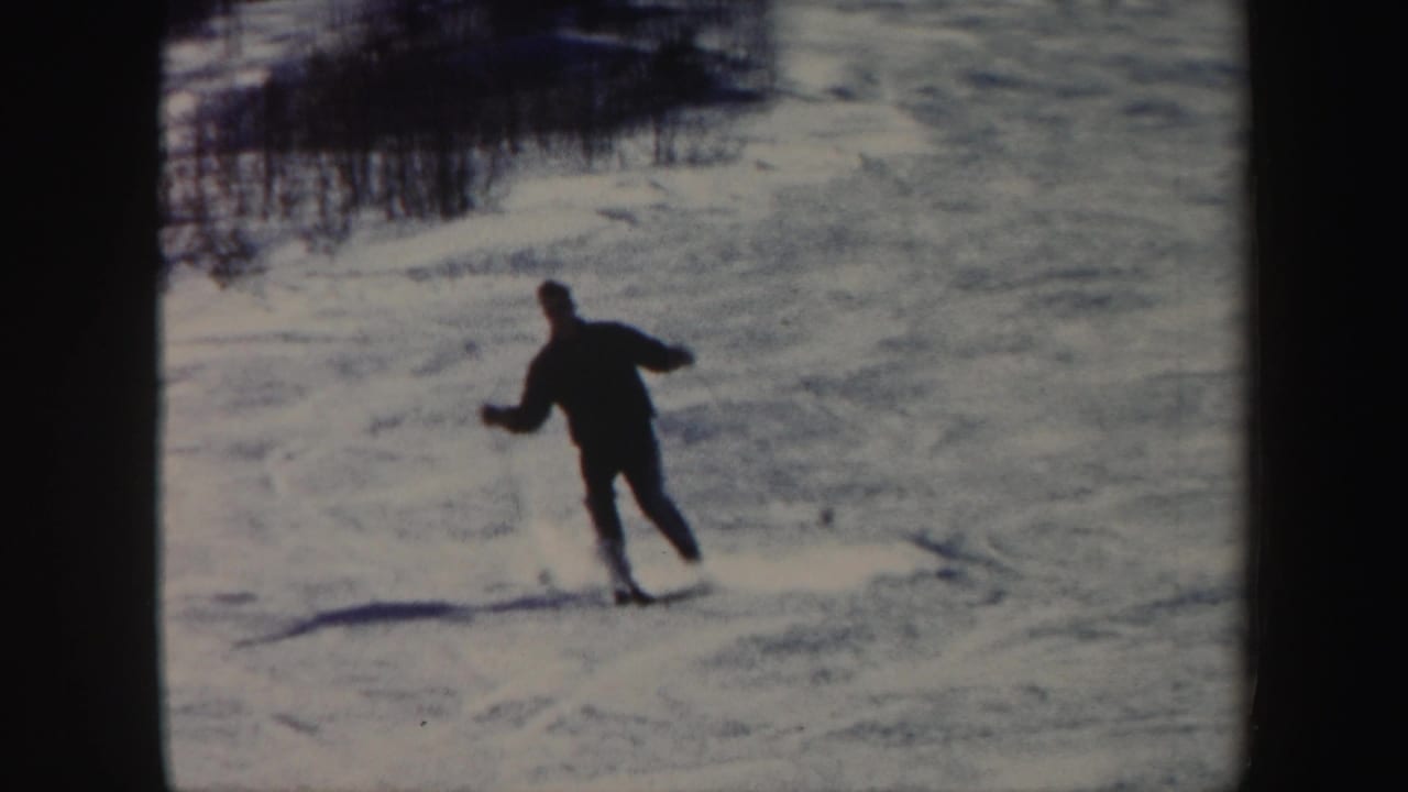 A skier in dark winter clothing moves downhill on a snowy Vermont slope in 1962 home-movie footage.