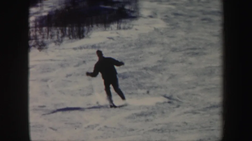 A skier in dark winter clothing moves downhill on a snowy Vermont slope in 1962 home-movie footage.