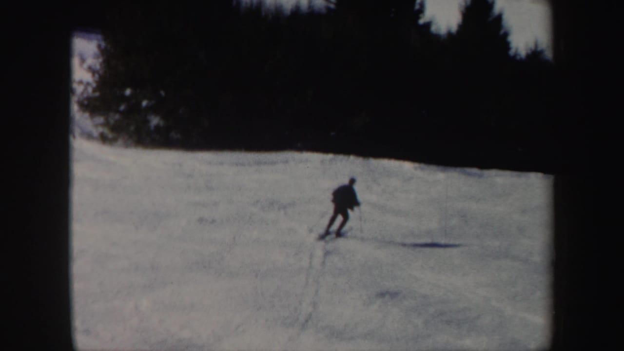 Lone skier crossing a snowy slope with dark trees in the background.
