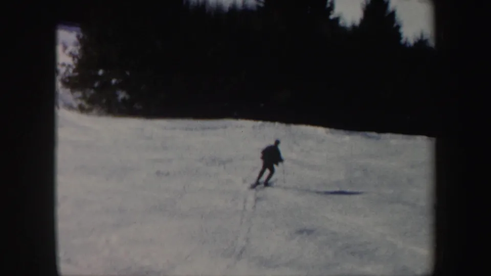 A distant lone skier in dark winter clothing glides across a snowy Vermont slope in 1962 home-movie footage.