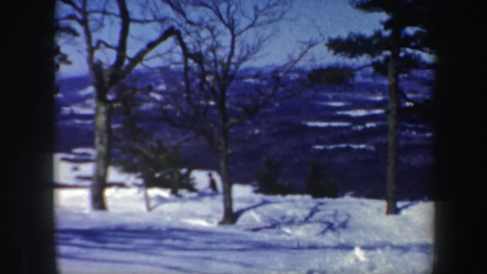 A quiet Vermont winter landscape shows snow-covered foreground, leafless trees, and distant hills under a blue sky.