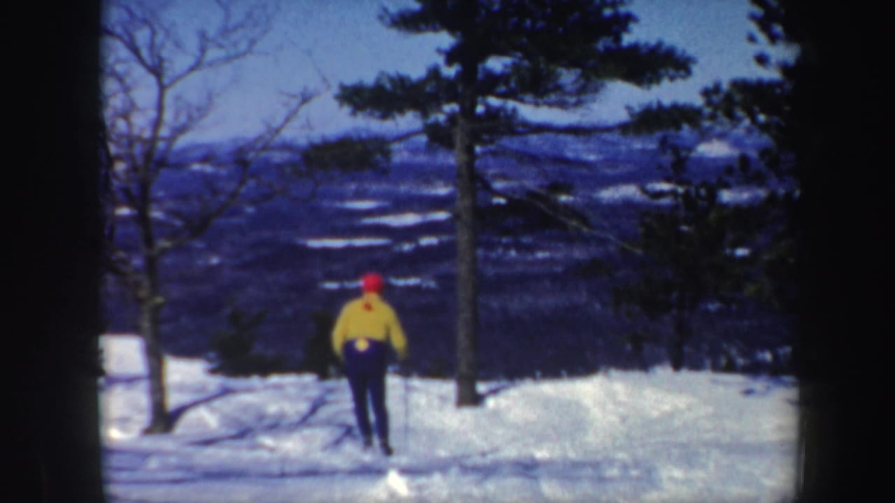 1962 Vermont winter footage frame with the skier receding toward the center of a snow-covered hill below a mountain view.
