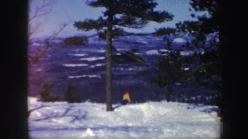 Final 1962 Vermont frame showing the skier as a small figure on the snow, with trees and blue mountain ridges in the background.