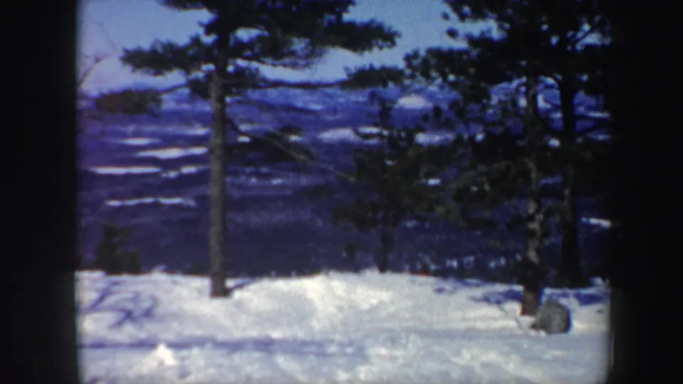 1962 Vermont 8mm view of a snowy ski area framed by evergreens, with distant winter hills beyond the slope.