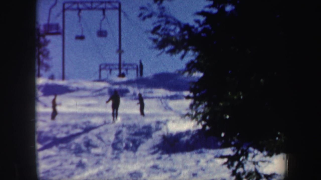 1962 Vermont ski-resort scene with skiers on the snow and a lift structure visible near the top of the hill.