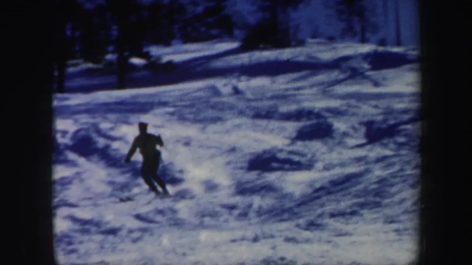 1962 Vermont ski footage with a skier turning across the snow, framed by trees and blue-toned 8mm film texture.