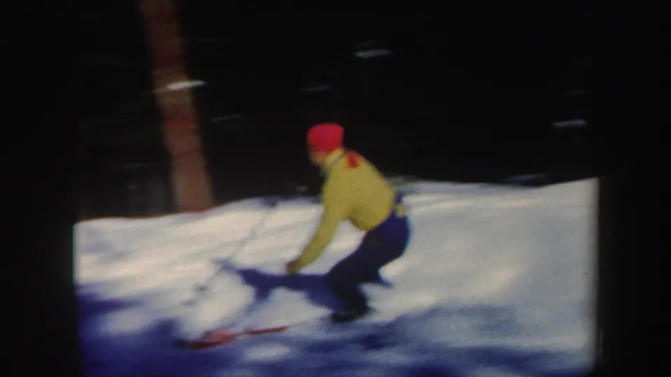 The skier crouches through a turn on a snowy wooded slope in 1962 Vermont home-movie footage.