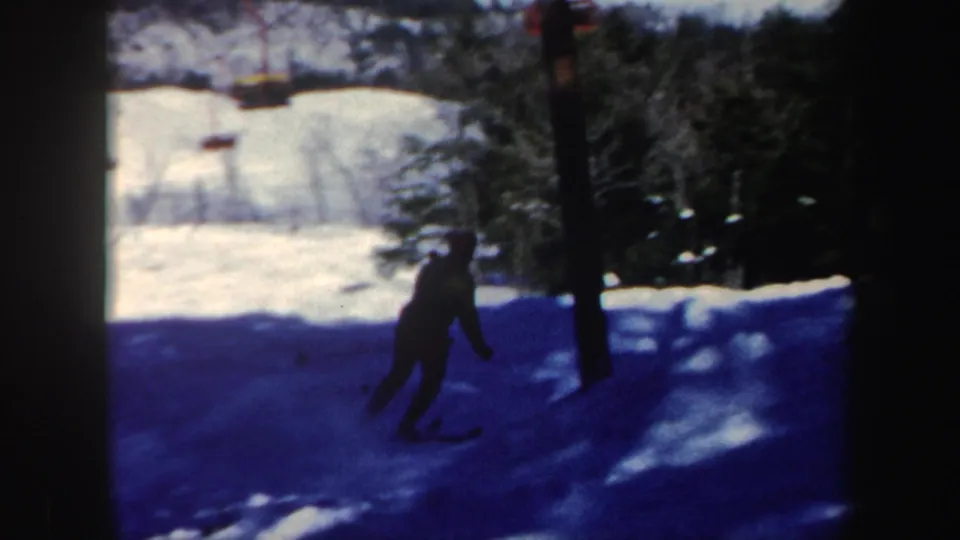 A distant skier descends a shaded Vermont slope with trees and a lift structure visible in 1962 footage.