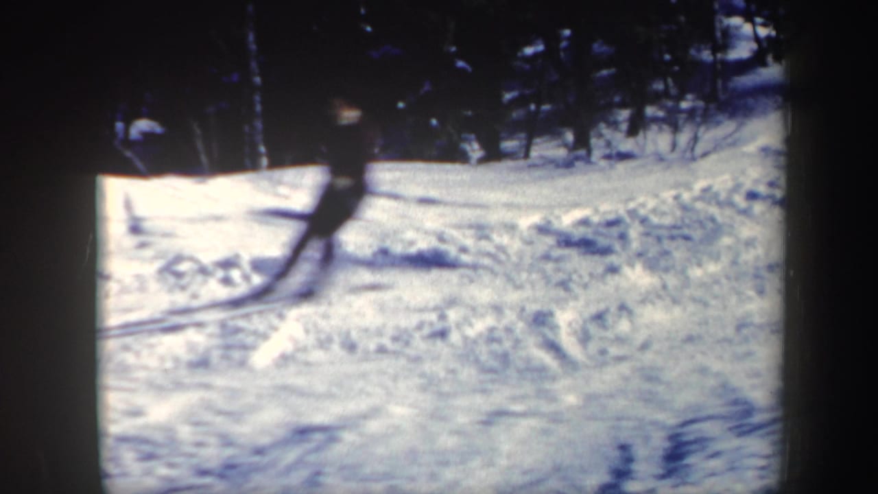 Snowy wooded slope with a skier partly visible at the left edge.