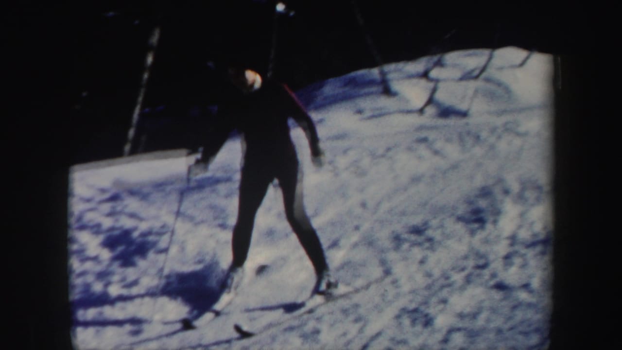 Skier in dark pants and a light hat glides downhill on a snowy slope.