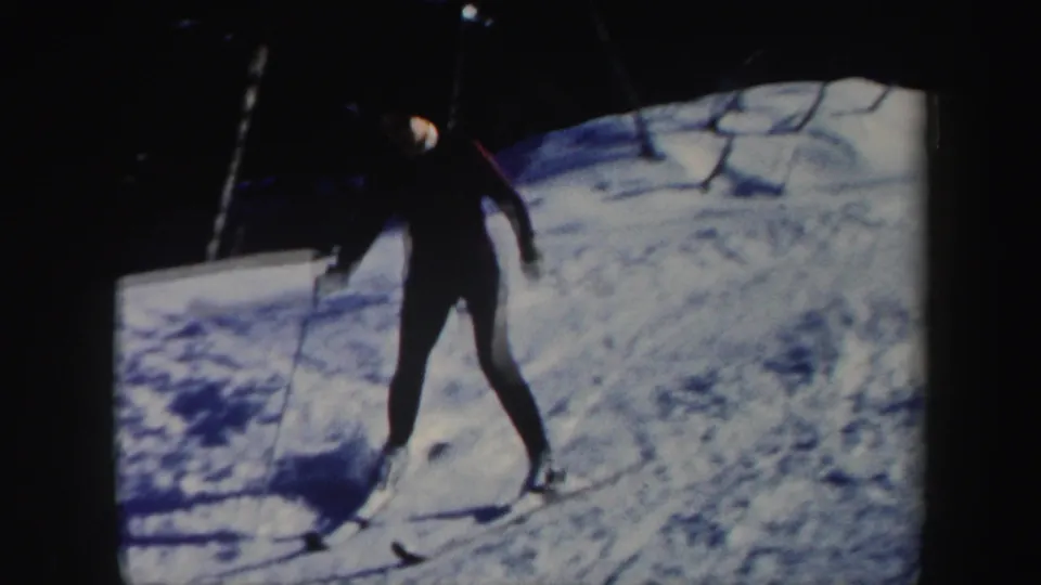 A woman skier in a maroon top, dark pants, and light hat moves downhill on a snowy Vermont slope in 1962 footage.