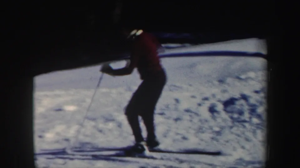 The woman skier appears to slow or pause on skis on a snowy Vermont hillside, with bright snow and dark trees behind her.
