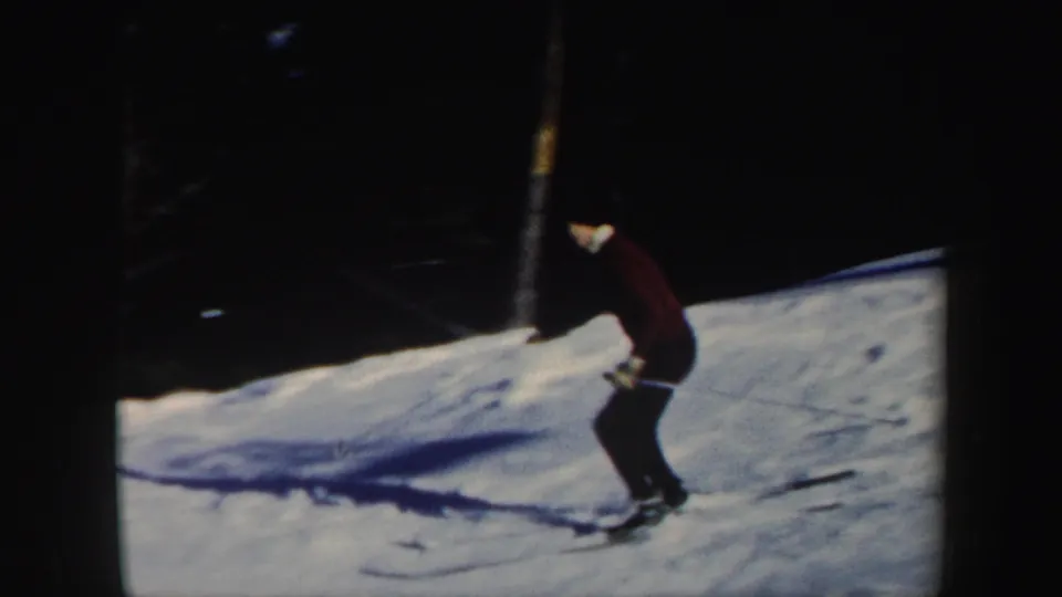 A woman skier in a maroon top bends into her descent on a snowy wooded Vermont slope in 1962 8mm footage.