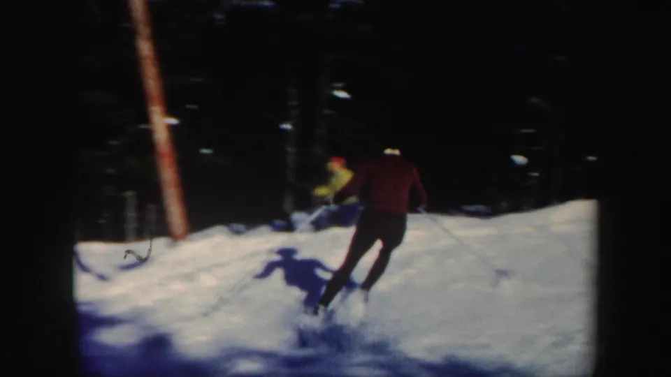 1962 Vermont home-movie frame showing a skier in a red jacket crossing a snowy slope among dark trees.