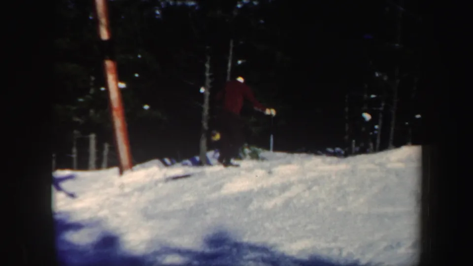 1962 Vermont frame with a skier near the edge of a snow-covered slope bordered by dark forest.