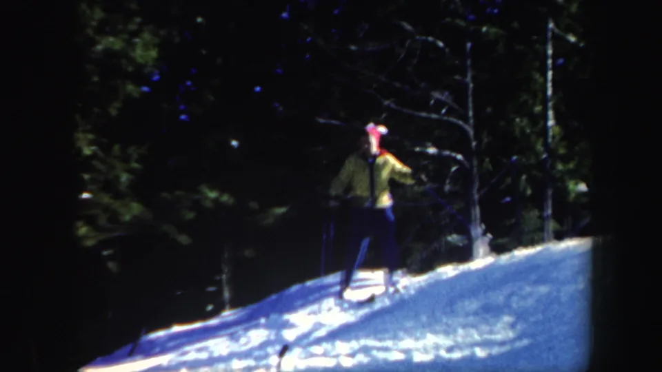 1962 Vermont home-movie frame showing a skier in yellow clothing and red hat on a snowy wooded incline.