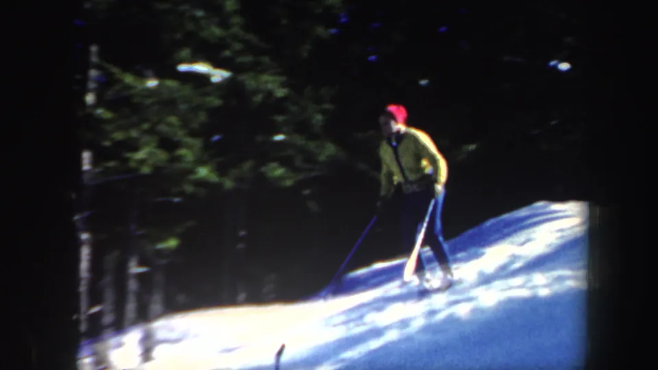 1962 Vermont frame showing a yellow-clad skier with poles moving across a bright snowbank near dark trees.