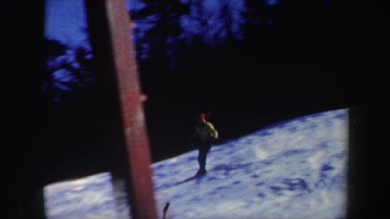 1962 Vermont 8mm frame with a skier in a yellow jacket and red cap descending a snowy slope near dark trees.