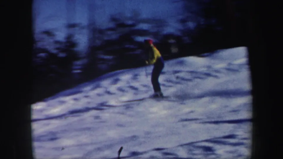 1962 Vermont home-movie frame showing a yellow-jacketed skier gliding across a blue-toned snowy hillside.