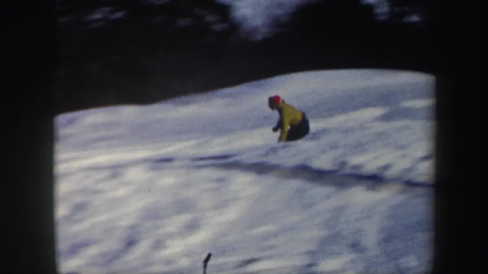 1962 Vermont 8mm frame showing the skier crouched low while descending a bright snow-covered slope.