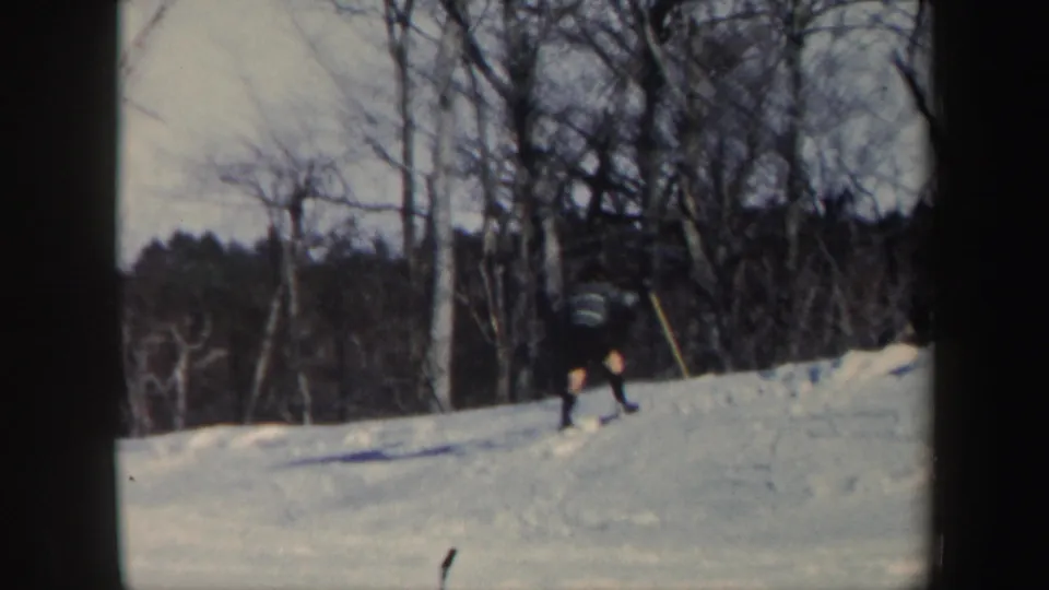 A distant skier moves across a snowy Vermont slope in 1962 home-movie footage, with bare trees behind them.