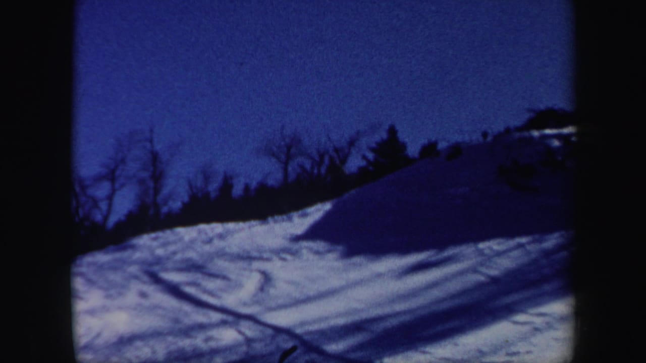 A blue-toned view of the snowy Vermont hillside shows ski tracks and dark trees along the upper edge.