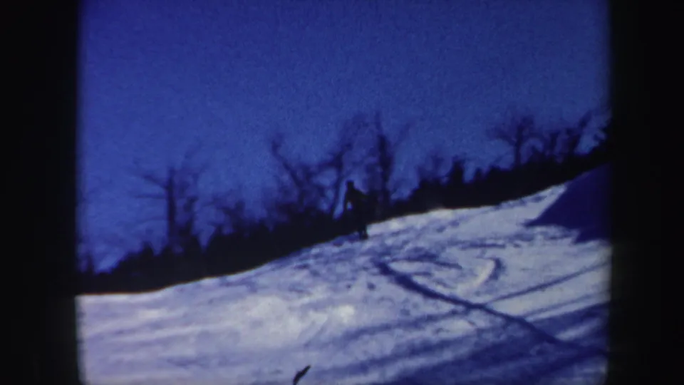 A small skier figure appears on the blue-toned snowy slope, with curved tracks cutting across the foreground.