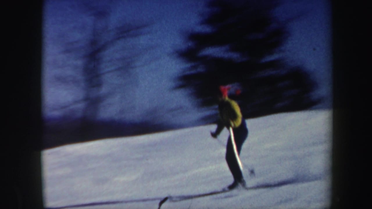 A skier in a yellow jacket and red hat crosses a snowy Vermont hillside in grainy 1962 8mm footage.