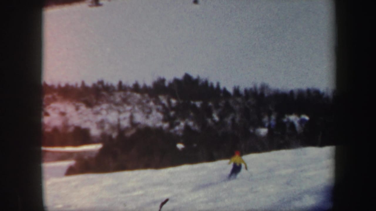 Skier in a bright jacket descends a snowy slope with trees in the background.