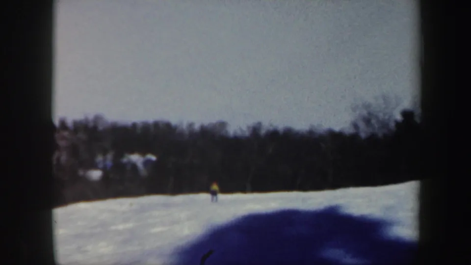 1962 Vermont 8mm frame showing the skier small in the distance on a broad snowy slope with wooded background.