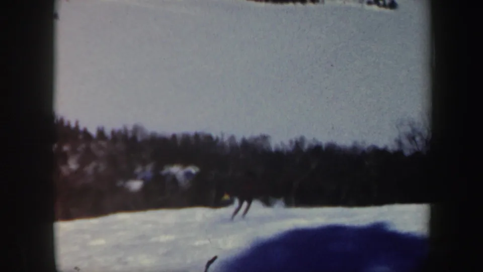 1962 Vermont 8mm frame showing distant skiers crossing a snowy slope below a dark tree line.