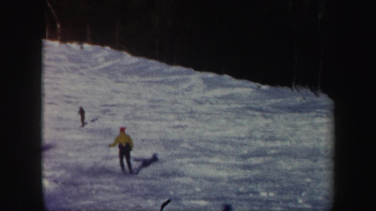 A distant skier in a yellow jacket continues down a Vermont snow slope, with another small figure visible farther uphill.