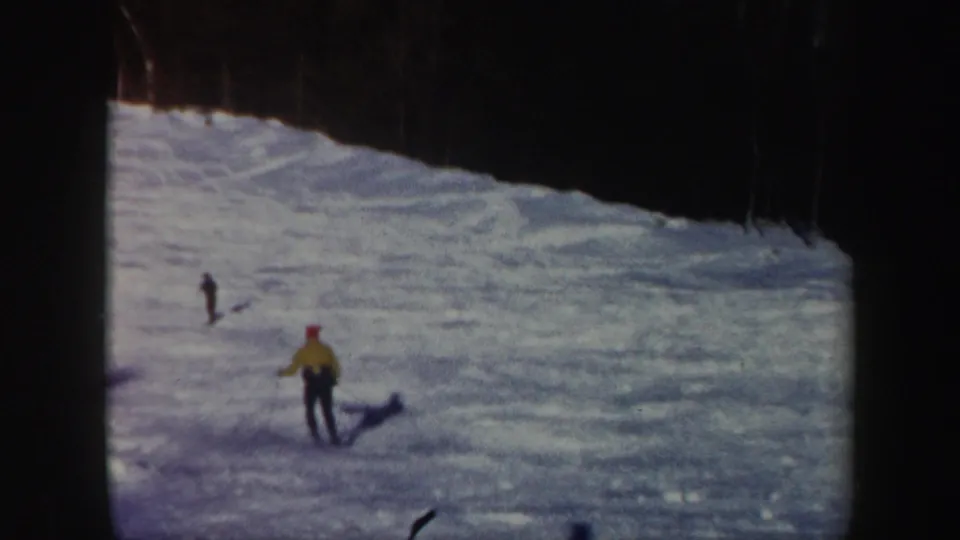 A distant skier in a yellow jacket continues down a Vermont snow slope, with another small figure visible farther uphill.